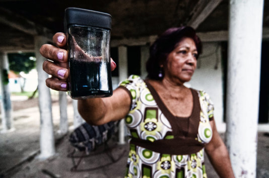 Elena Riquer, a Capoacán neighbour, shows the water she collected in a glass from the roof of her home after raining, blackend by the pet coke smoke.