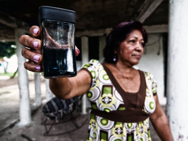 Elena Riquer, a Capoacán neighbour, shows the water she collected in a glass from the roof of her home after raining, blackend by the pet coke smoke. Elena Riquer, a Capoacán neighbour, shows the water she collected in a glass from the roof of her home after raining, blackend by the pet coke smoke.