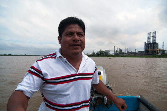 Juan Luis Francisco in a boat on the Coatzacoalcos river with the pet coke processing plant behind him.
