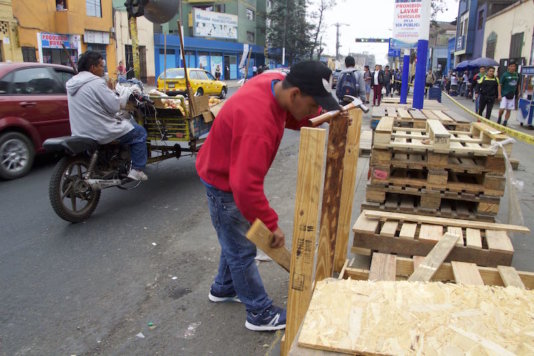 A volunteer prepares pallets to build a bus stop in a bustling avenue.