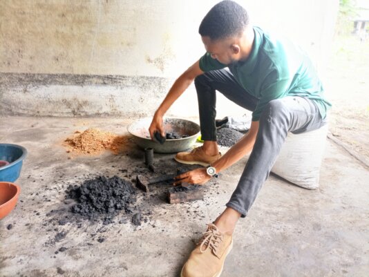Mboza Clinton pounding mixture into a manual moulding mahchine to produce charcoal briquettes.